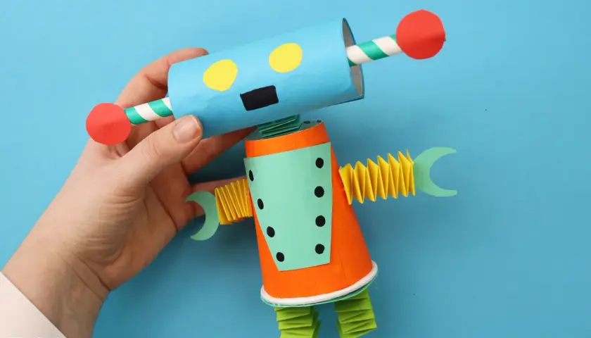 Ein bunter Roboter, der zum **Roboter basteln** einlädt. Er hat einen blauen Kopf mit gelben Augen und einen orangefarbenen Körper.