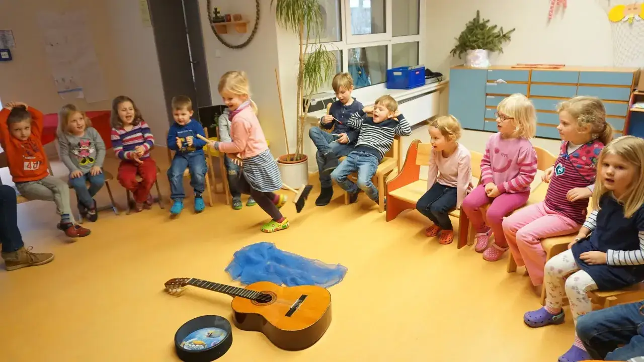 Kinder sitzen im Kreis, ein Mädchen fegt mit einem Besen. Tip tap, die Musik beginnt.