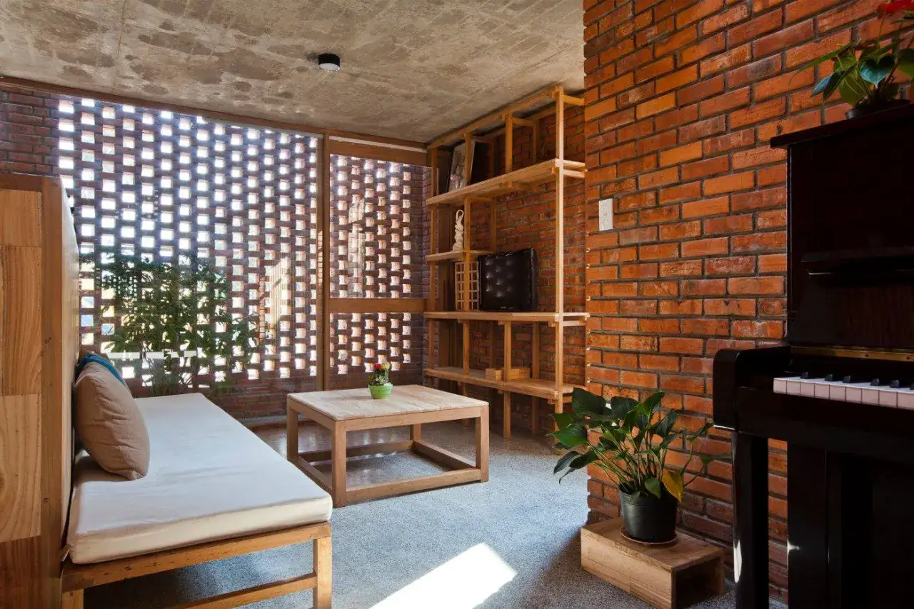 Gem&uuml;tliches Wohnzimmer mit Holzb&auml;nken, einem Holztisch und einem Klavier. Die Wand aus roten Ziegeln und die Fenster mit moc klemmbausteine-Muster schaffen eine warme Atmosph&auml;re.