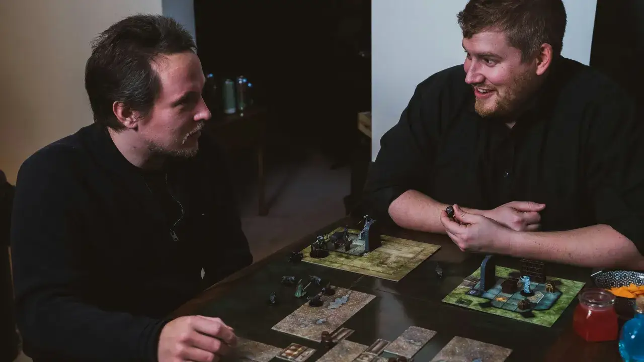 Zwei Freunde spielen ein episches Abenteuer. Sie sind vertieft in eines der besten 2 Spieler Brettspiele, mit Miniaturen und W&uuml;rfeln auf dem Tisch.