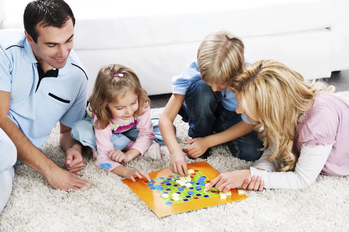 Familie spielt Brettspiel. Vater, Mutter und zwei Kinder sitzen auf dem Teppich und sind vertieft in ein spannendes party spiel.
