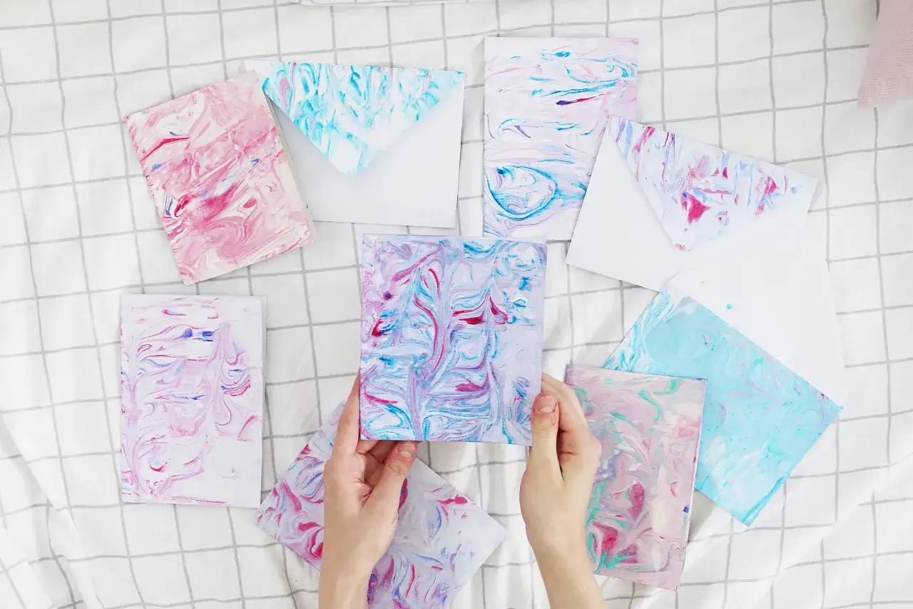Bunte Karten und Umschl&auml;ge mit Marmorierungsmuster, die an flie&szlig;endes Wasser erinnern. Papier marmorieren ist eine kreative Technik.
